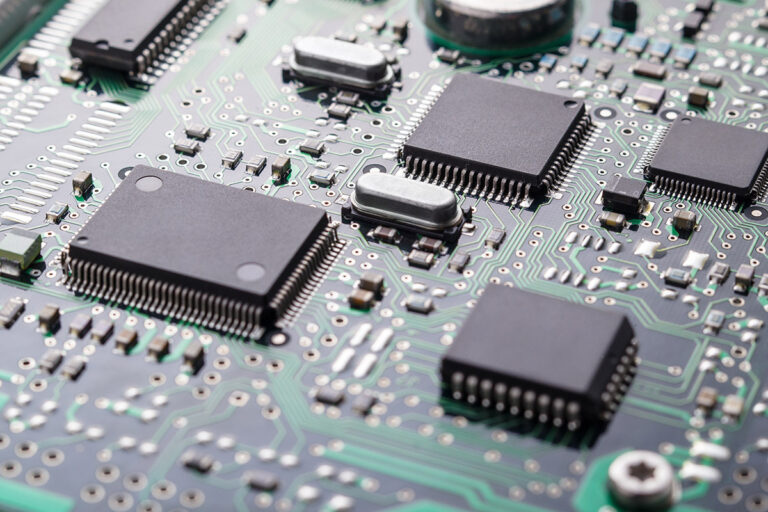 Close-up of a green circuit board with multiple black microchips and metallic components, showing intricate pathways and a high-tech, organised design.