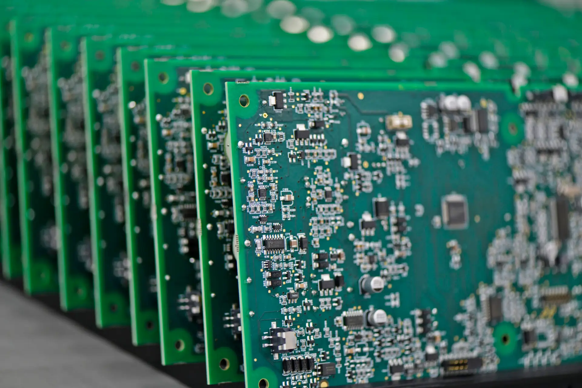 Close-up of stacked green circuit boards with intricate silver components, highlighting advanced technology and precision manufacturing. PCB Assembly