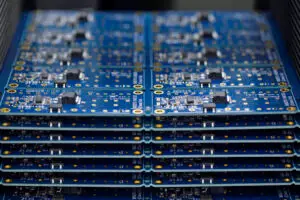 Stack of blue printed circuit boards with various electronic components and gold contacts. The arrangement is orderly, highlighting technology precision.