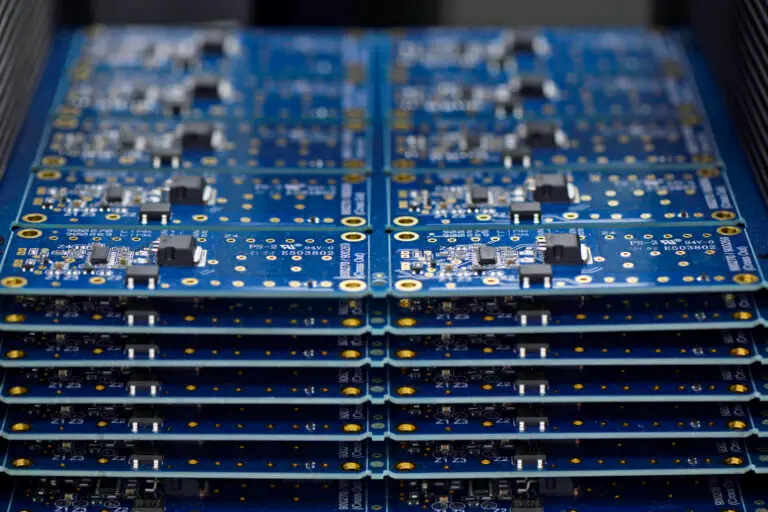 Stack of blue printed circuit boards with various electronic components and gold contacts. The arrangement is orderly, highlighting technology precision.