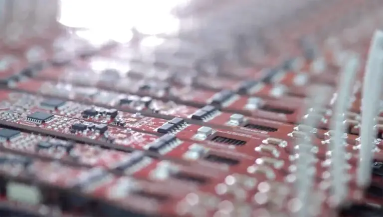 Close-up of a red circuit board with black and white components. The image is focused on the intricate details, reflecting a high-tech, intricate design.