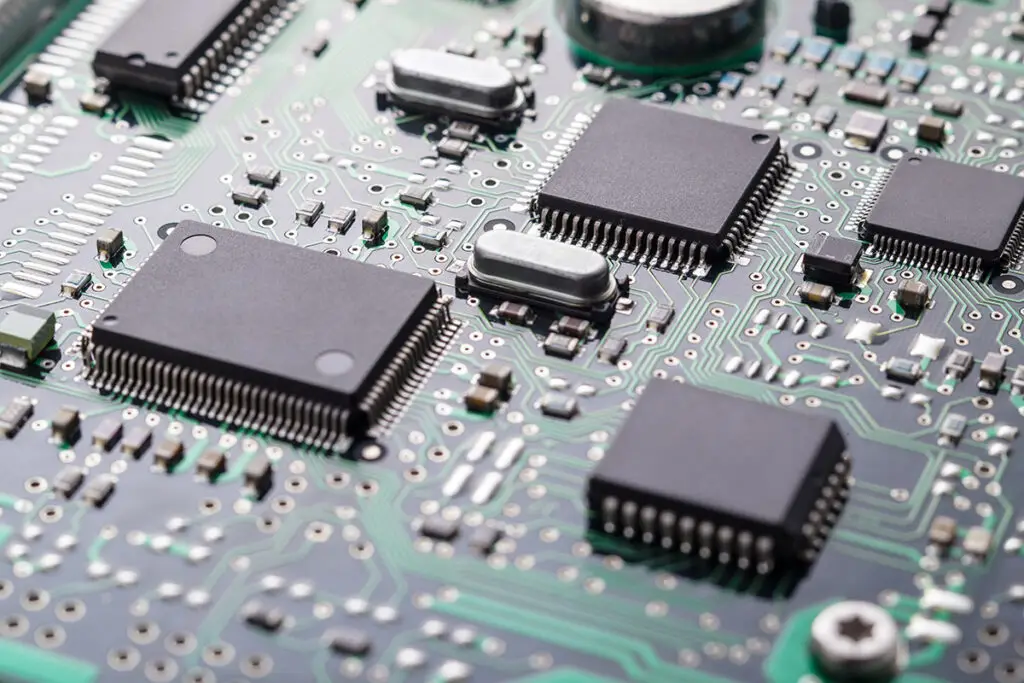 Close-up of a green circuit board with multiple black microchips and intricate silver pathways, conveying a sense of modern technology and complexity.