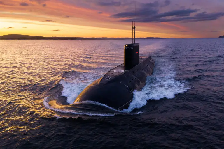 A submarine cruises on open water against a vivid sunset, casting orange and purple hues across the sky and sea; the scene feels serene and powerful.