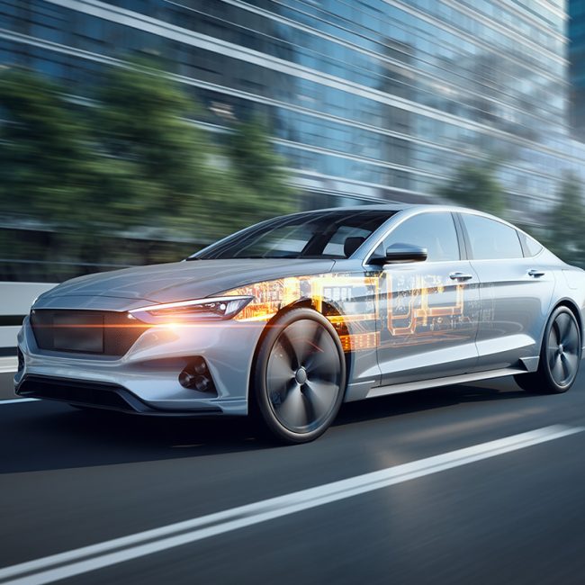 A sleek silver car speeds through a city street, with digital overlays of circuitry on its side, showcasing futuristic technology and innovation.