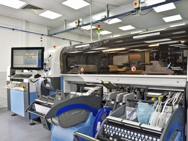 Industrial machine in a factory with complex parts, panels, and a computer interface. The setting is clean and modern, conveying efficiency.