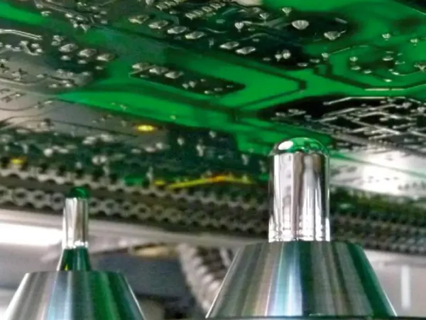 Close-up of a green circuit board above a selective soldering machine in a manufacturing setting. The scene conveys precision and advanced technology.