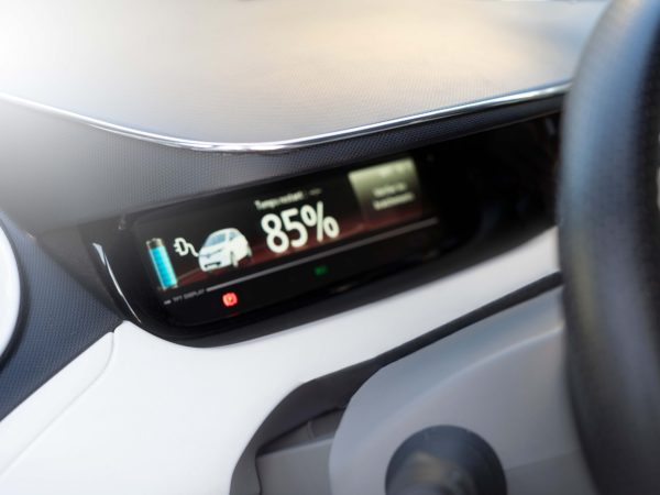 Close-up of an electric car dashboard displaying a battery charge at 85% with icons, set against a modern, sleek interior design.