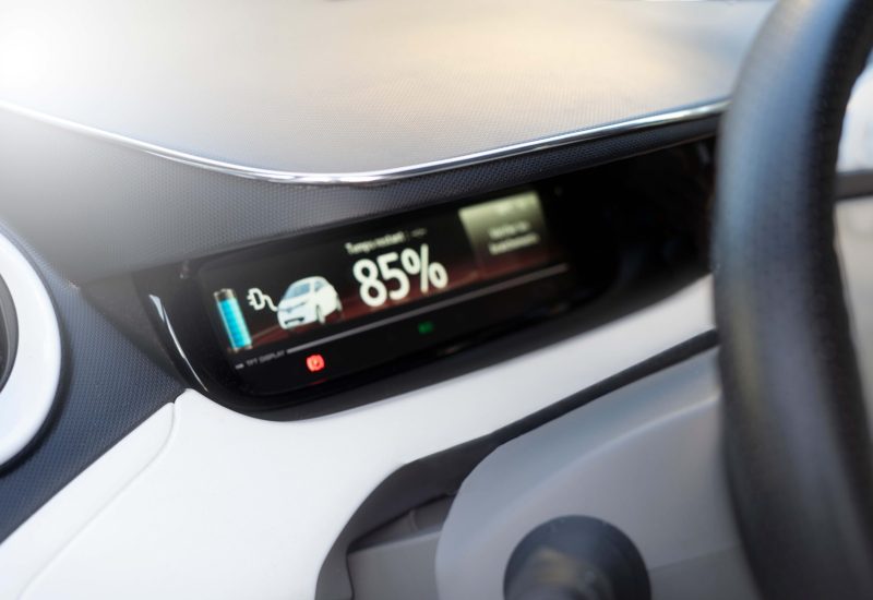 Close-up of a car dashboard displaying an electric vehicle's battery charge at 85%. The background shows a digital screen with a battery icon.