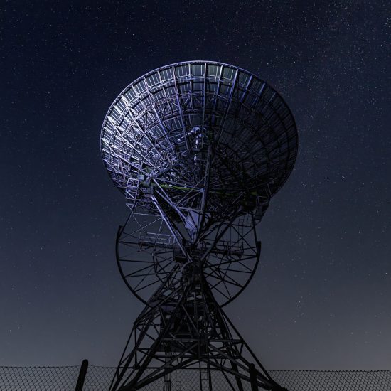 Satellite dish silhouetted against a starry night sky, with its metal structure illuminated subtly. The image conveys a sense of exploration and mystery.